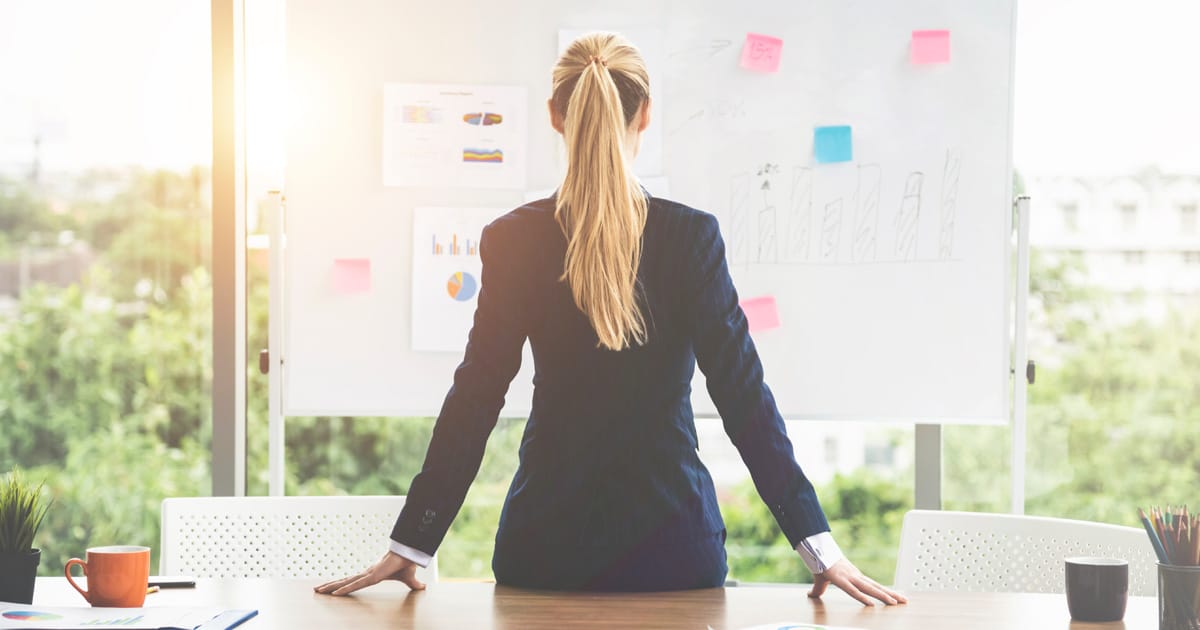 Business woman sitting on a desk staring at a white board.