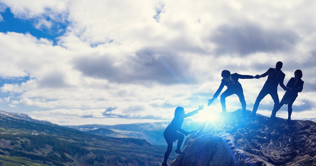 Silhouette of four people climbing mountain holding hands.